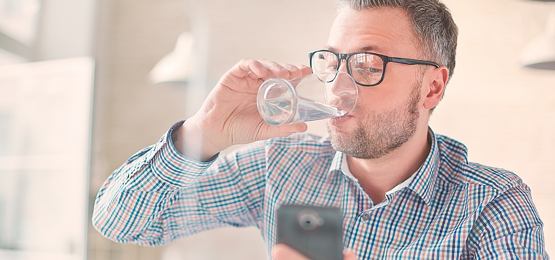 Mand drikker et glas vand, mens han kigger på sin mobil